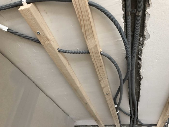 Elinstallation med kablar draget längs träreglar och genom flexibla rör i betongvägg under renovering.
