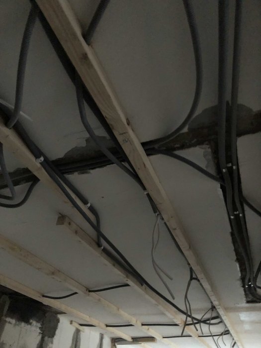 Bild på elinstallationer och kablar fastsatta längs takbjälkar under renovering.