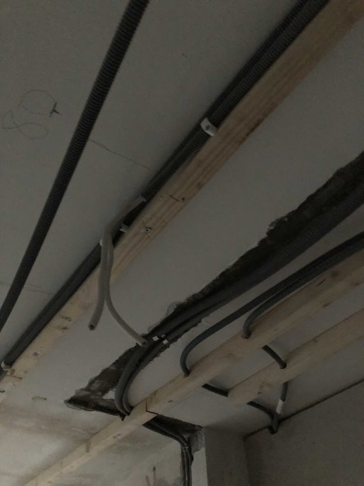 Elledningar och rör draget längs träreglar under ett betongtak i pågående installation.