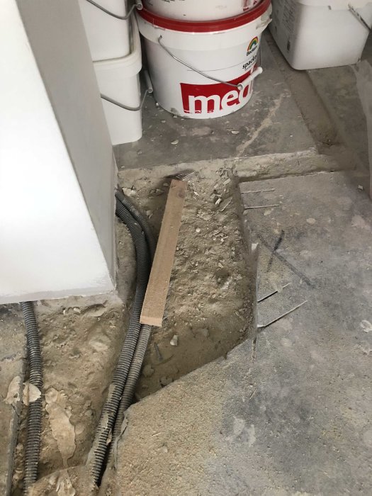 Betonfußboden mit offener elektrischer Leitung und Mauerwerk, umgeben von Bauwerkzeugen und Eimern.