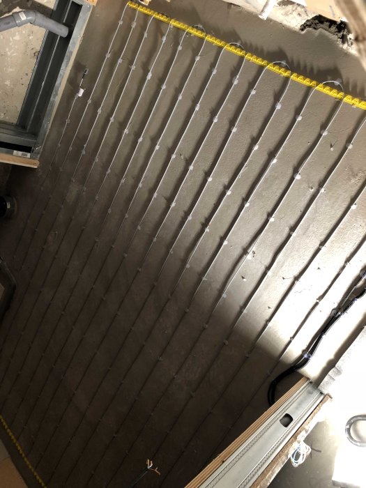 Golvvärmerör installerade i system innan betonggjutning, med tavelmåttband för skala.