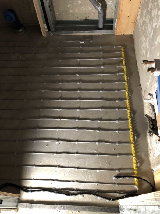 Installation av golvvärme med synliga rör och fästklammer på betonggolv, måttband längs sidan.