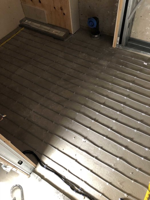 Installation av golvvärme med synliga värmeslingor på ett betonggolv i ett byggprojekt.