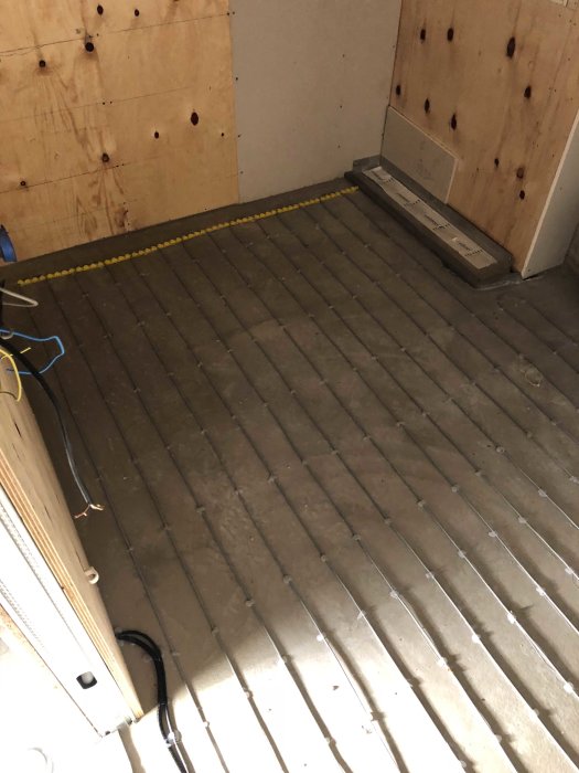 Golvyta med måttband, oskyddade elkablar och oisolerade väggar i ett pågående renoveringsprojekt.