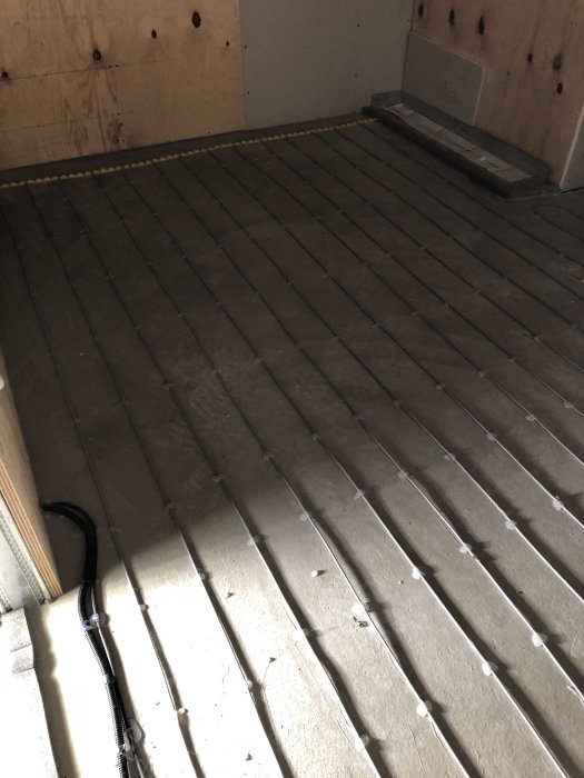 Oisolerad trägolvkonstruktion med spår för golvvärme och elinstallationer synliga.