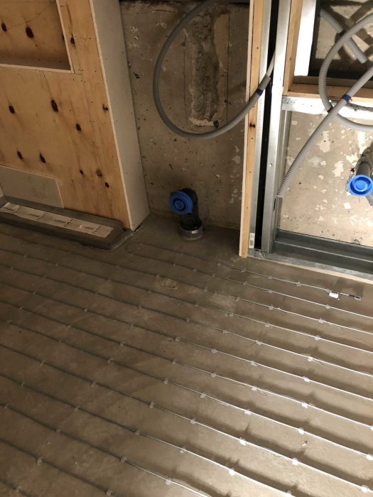 Renoveringsarbete med synliga VVS-installationer och värmegolvsslangar på betonggolv.