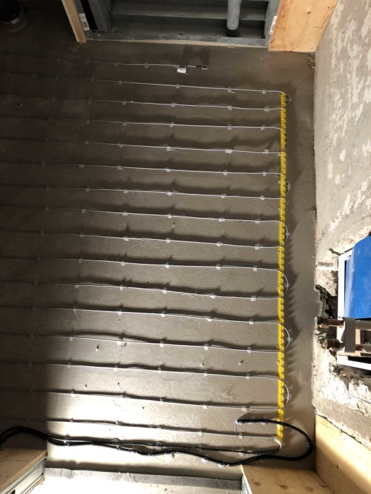 Installation av golvvärme med synliga rör och fästen på ett betonggolv under renovering.