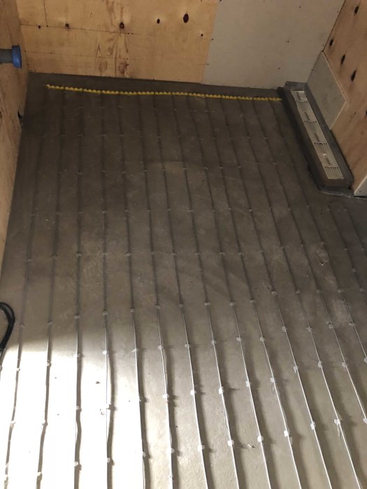 Installation av golvvärme med synliga värmeslingor på betonggolv i ett pågående byggprojekt.