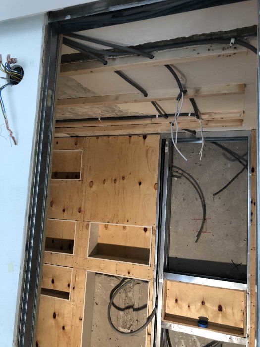 Delvis installerad elektrisk infrastruktur och isolering i en vägg under konstruktion.