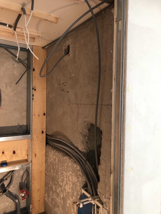 Betongvägg med elektriska ledningar och rör under konstruktion, markerade mätningar, och trästöd.