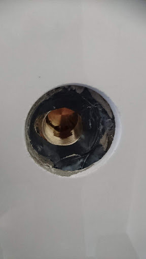 En duschkraninstallation med en synlig kopparplugg omgiven av tätskikt och svart manschett i en vit kaklad vägg.