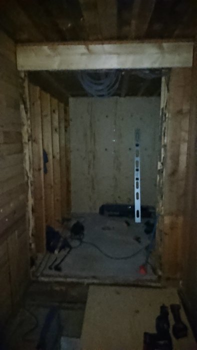 En mörk byggplats med träreglar och OSB-skivor, en vattenpass och byggverktyg syns, i väntan på renovering.