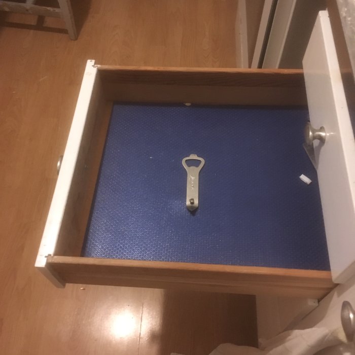 Öppen låda med en blå matta och en ensam flasköppnare i mitten, mot en bakgrund av ett trägolv.