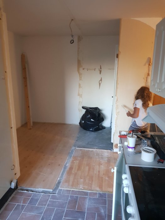 Renoveringsprojekt med olika golv och väggar under demontering i ett kök som leder in till en hall.