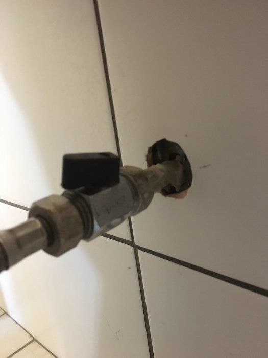 Vattenrör som sticker ut genom en vit kakelvägg med en dåligt tätad öppning runt röret.