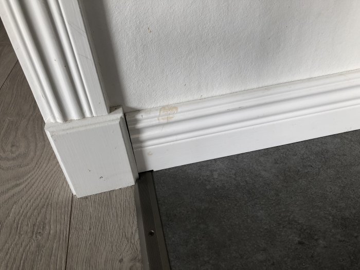 Vit dörrkarm och golvlist som inte passar perfekt i hörnet, tecken på en DIY-renovering.