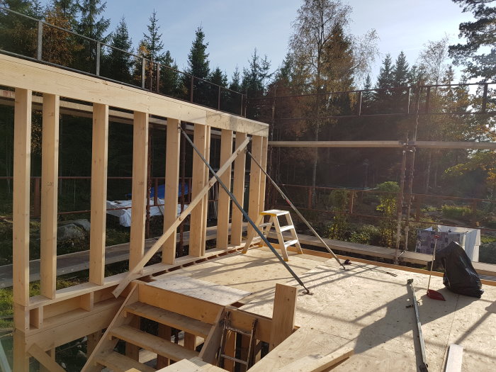Nybyggd trästomme för vägg med väggstämp, limträbalk över fönsterparti och pelare i hörn på byggarbetsplats.