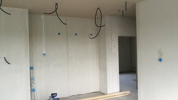 Omålade väggar i ett pågående byggprojekts korridor med elinstallationer och märkningar.