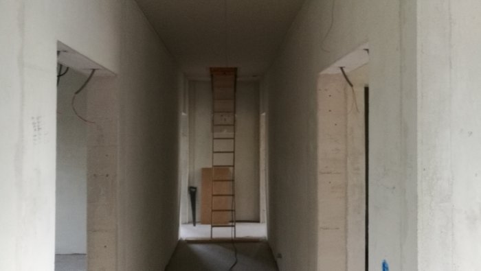 Korridor under konstruktion med synliga kablar och vit väggar som leder till ett rum.