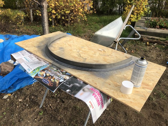 Spraymålning av svart bleck till silvergrå på en plywoodskiva utomhus vid renoveringsprojekt.