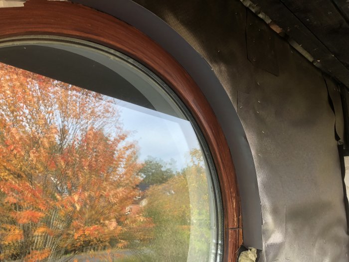 Ny målad panel runt fönster och silverfärgat plåtbleck med höstträd reflekterat i fönstret.