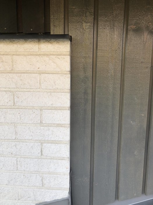 Nyinstallerad grå panel vid husentré bredvid vit tegelvägg, metalldetaljer och överbleck målade för att matcha.