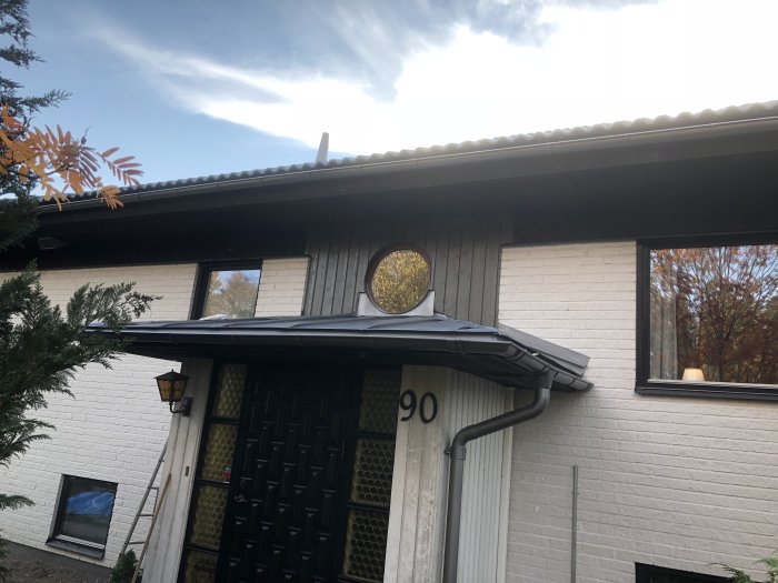 Nyinstallerad panel vid entré med silver/grå takplåtar och målat överbleck ovanför fönstret.