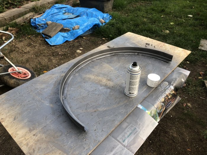 Spraymålning av bågformade metallbleck på träskiva, sprayburk och skyddspapper synliga.