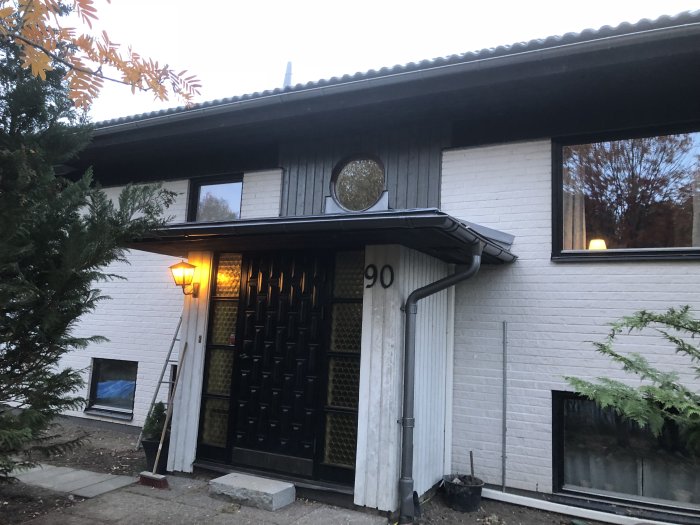 Husentré med ny panel, målat överbleck ovanför fönstret och silvergrå plåtdetaljer, takfot synlig.