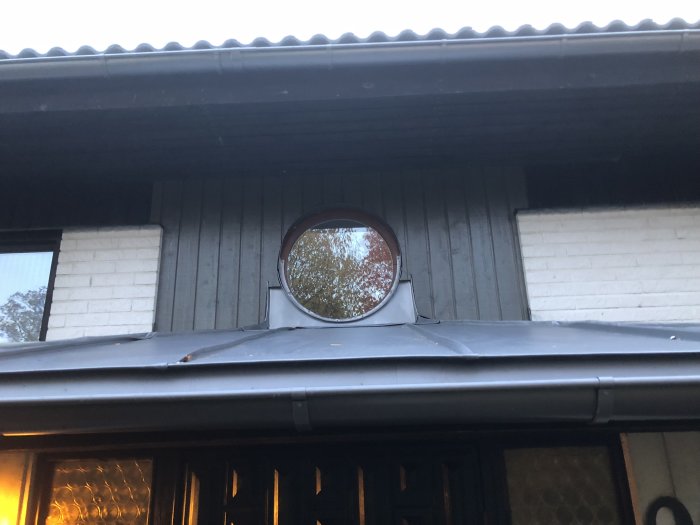 Målat överbleck ovanför ett rundat fönster på husfasad med ny lagt silvergråt plåttak och vattenbeständig tejp vid kanterna.