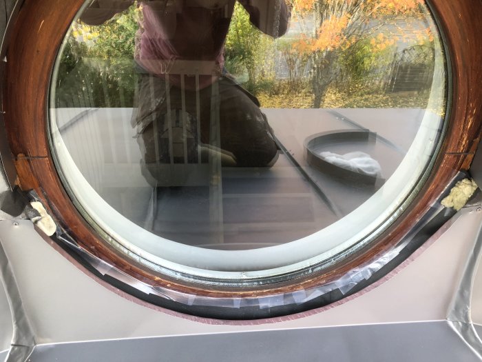 Nygjord panel vid en entré med ett rundat fönster och nyligen målat överbleck, reflektion av träd i glaset.