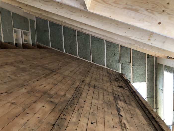 Renoverat rum med ny isolering på väggar, öppet tak med glespanel och synlig trägolv.