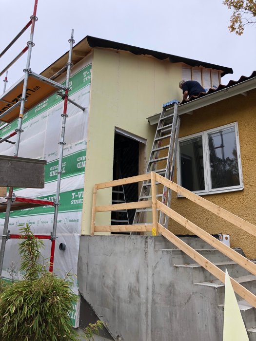 Renovering av hus med ny isolering och stomme, ställning och person som arbetar på taket.