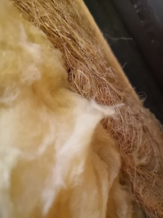 Närbild på äldre isoleringsmaterial som liknar unket gräs bakom en väggkarm.