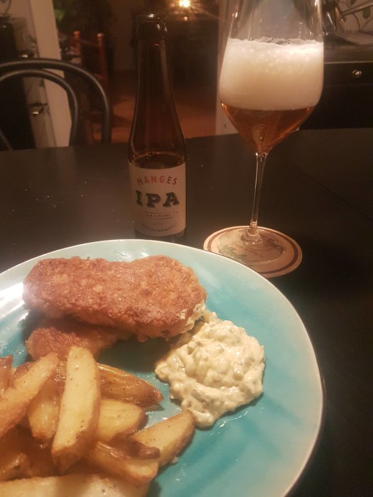 Flaska av Mänges IPA bredvid ett glas öl med skum, och en tallrik med schnitzel, pommes och remouladsås.