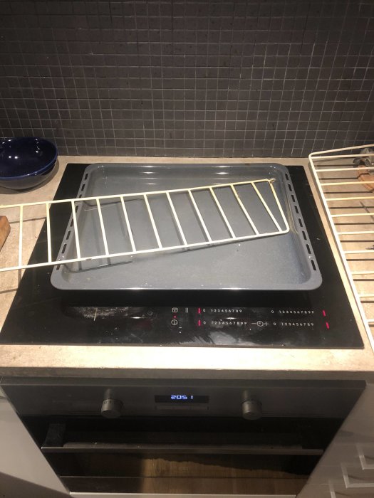 Ugn med öppen lucka och en bakplåt ovanpå en glaskeramikhäll.