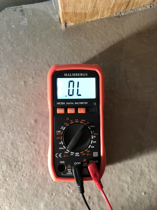 Digital multimeter med olika mätinställningar som visar 'OL' på displayen, ligger på ett betonggolv.