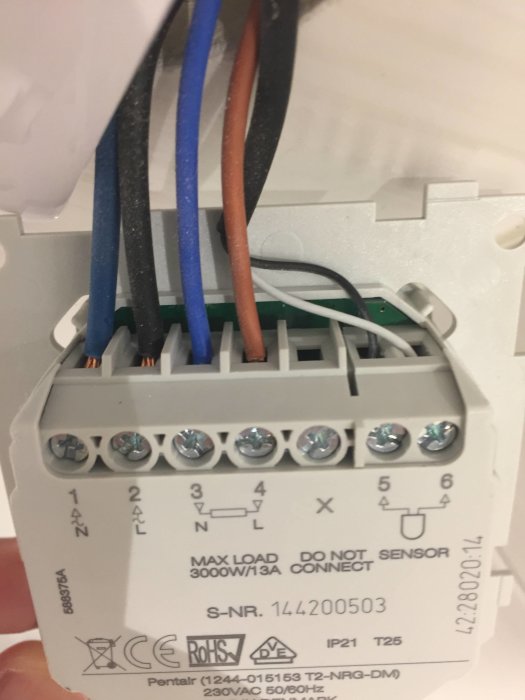 Närbild av en elektrisk givare med kopplade ledningar och märkning av anslutningar.