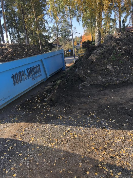 Grävningsarbete med stora högar av jord och en fylld container på en byggarbetsplats.