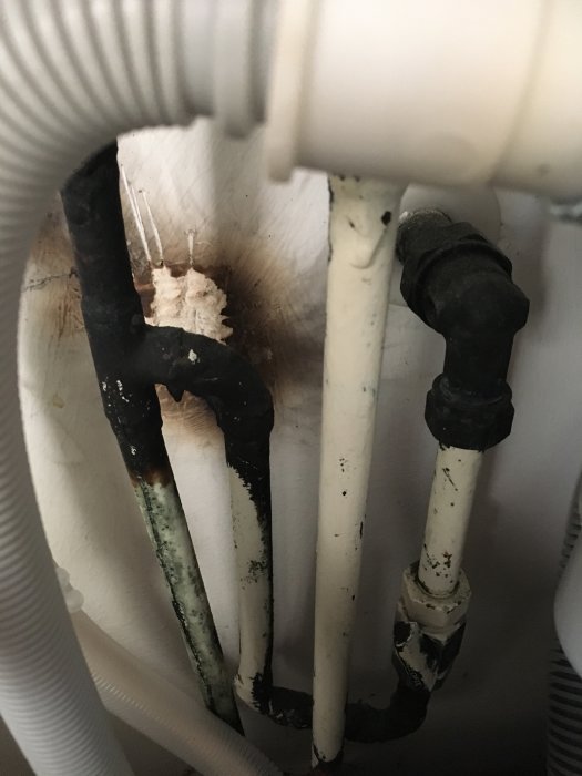 Rör under köksvask med tecken på korrosion och mögel, i ett äldre kök från 90-talet.