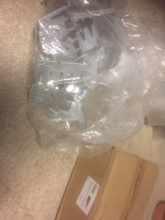 Överskott av nya spikplåtar och skarvplåtar i en plastpåse på ett betonggolv, bredvid en pappkartong.