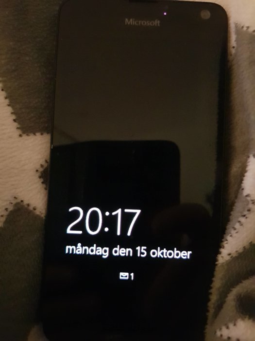 Svart Microsoft-mobiltelefon visar en skärmsläckare med digital klocka som anger tiden 20:17 och datumet måndagen den 15 oktober.