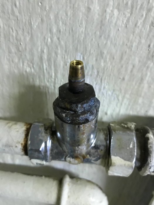Läckande termostatanslutning på ett radiatorrör med synliga droppspår och korrosion, behöver underhåll.