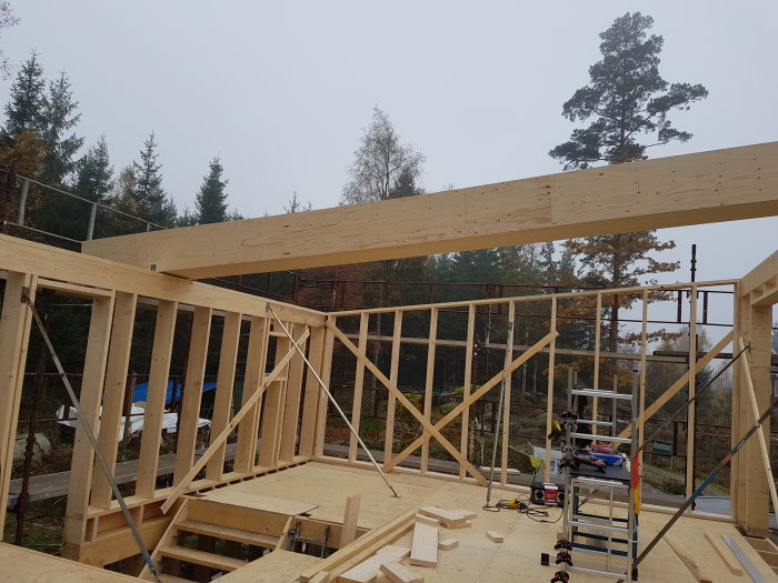 Upplyfta takreglar och väggstommar i trä på en byggarbetsplats med utspridda verktyg och sågat virke.