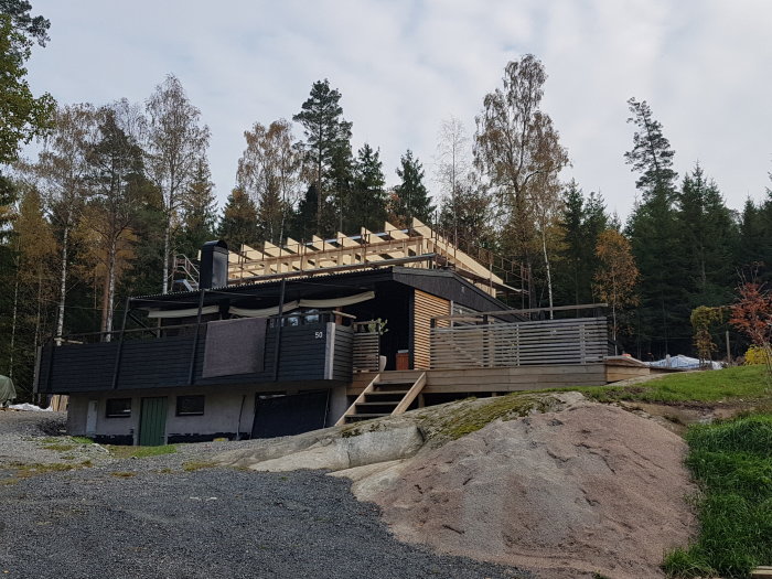 Hus under konstruktion med nya takreglar och utplacerade fönster på andra våningen, omgivet av träd.