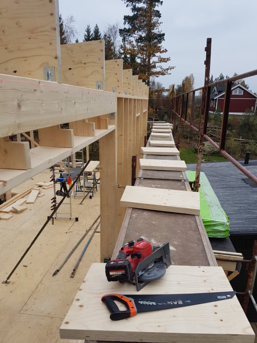 Byggplats för andra våningen med upplyfta takreglar och utplacerade träreglar, verktyg syns i förgrunden.