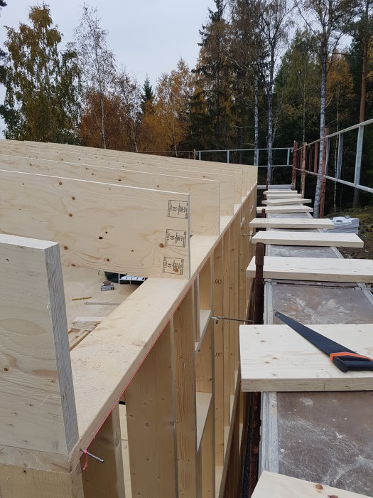 Upplyfta träreglar för takkonstruktion på en byggplats med kerto 51x450 mm, verktyg och träd i bakgrunden.