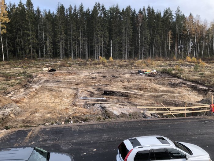 Nybyggnadsplats med uppgrävt markområde och berg, skog i bakgrunden, maskiner och material synligt.