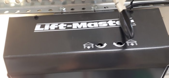 Svart garageportsmotor med vit text "Lift-Master" och symboler för garage, bil och hus på ytan.