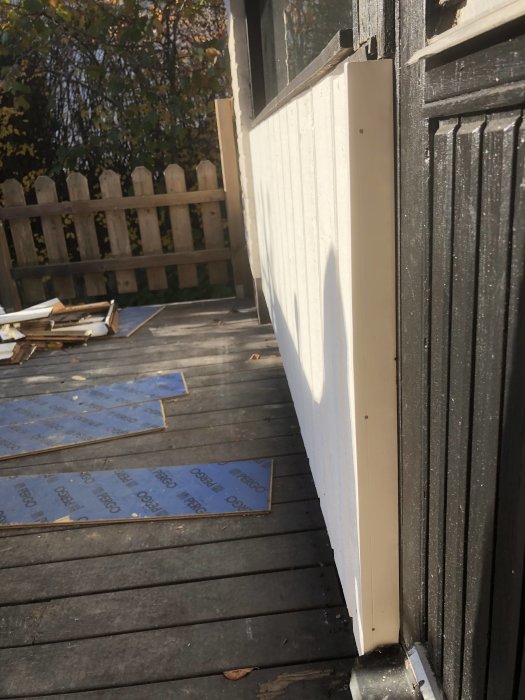 Nyinstallerad vit täckbit på panelen vid en altan, med osmålad trä och blå skyddsplattor synliga på golvet.